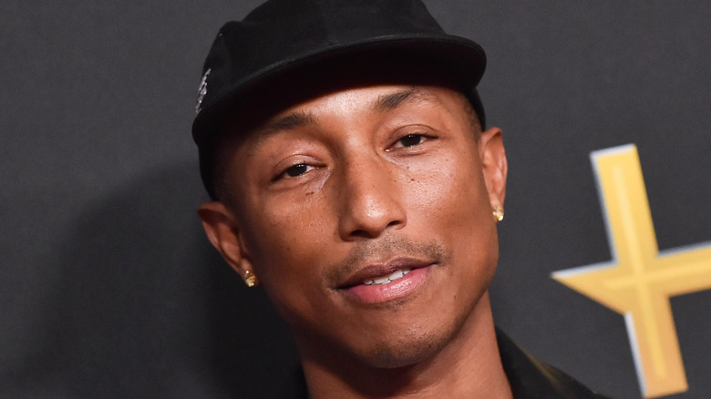 Pharrell Williams wearing black cap and half-smiling