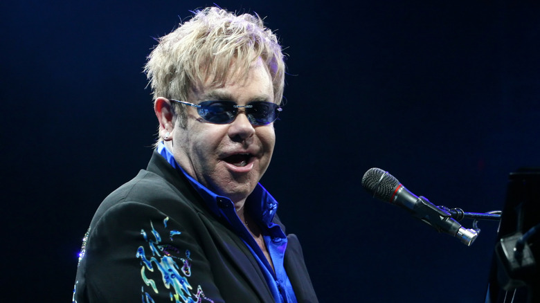 Elton John wearing sunglasses in front of a microphone