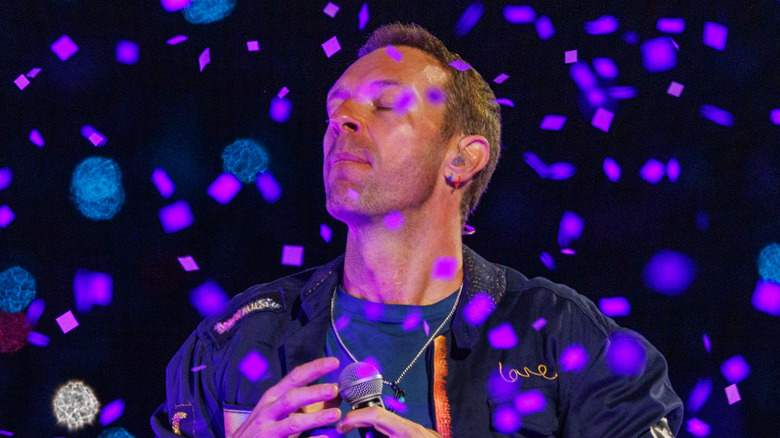 chris martin of coldplay performs and closes eyes on stage amidst confetti