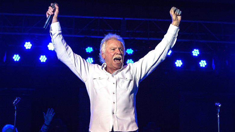 Joe Bonsall holding both arms in the air onstage