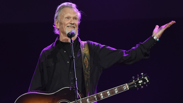 Kris Kristofferson gesturing holding a guitar onstage