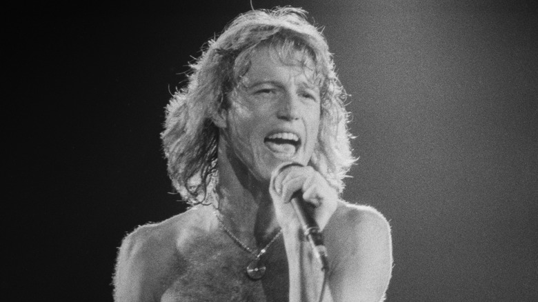 Andy Gibb singing into a microphone while shirtless onstage