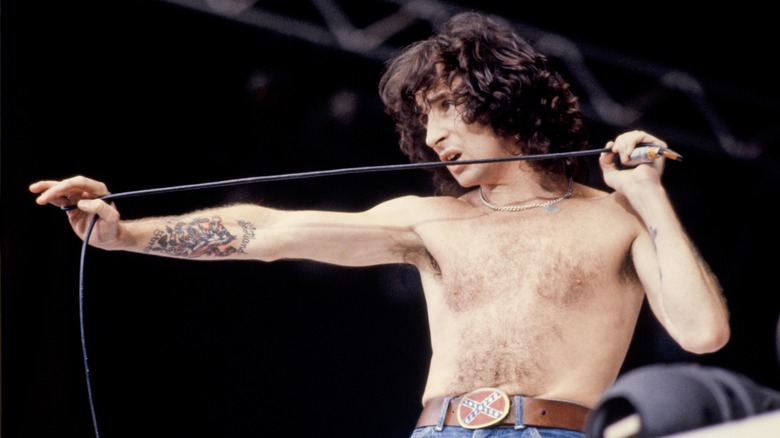 Bon Scott holding a microphone performing shirtless onstage