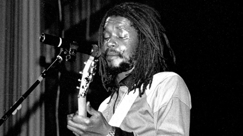 Peter Tosh playing guitar with eyes closed in front of a microphone