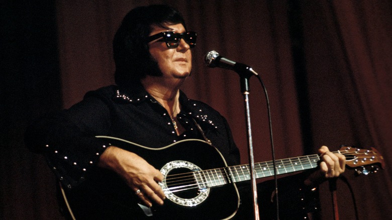 Roy Orbison playing guitar onstage in front of a microphone