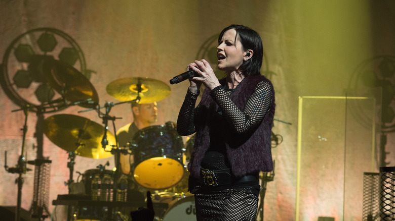 Dolores O'Riordan in fishnet singing in front of a drum kit