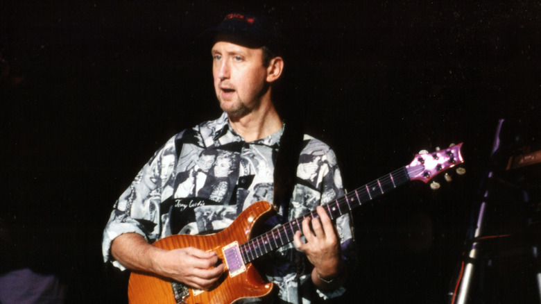 Ian Bairnson wearing a ball cap playing guitar onstage