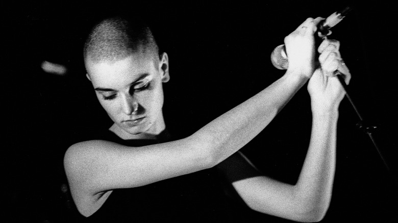 Sinead O'Connor looking downward holding a microphone =