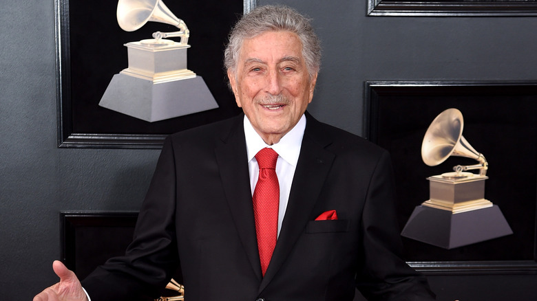 Tony Bennett in a suit with framed Grammy pictures