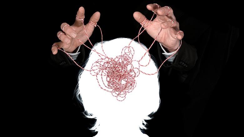 Hands holding tangle of string in a brain