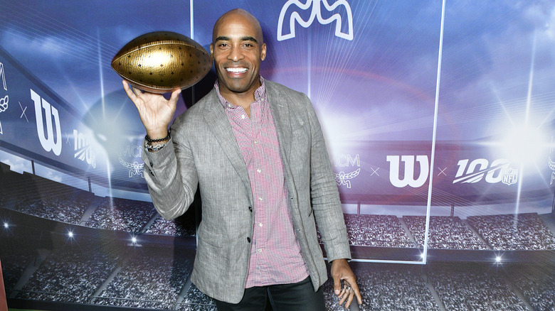 Tiki Barber posing at event holding up golden football