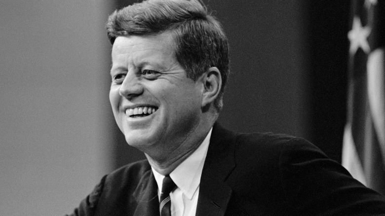 JFK smiles in front of flag