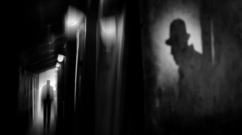 Silhouette of a man in a coat and hat in a dark alley