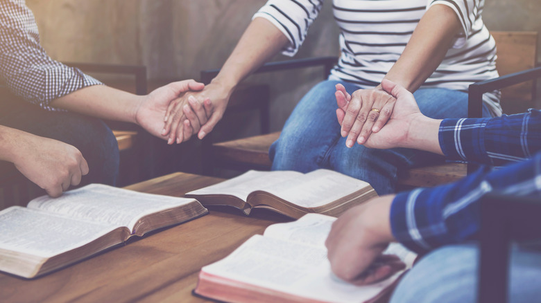 Christian small group holding hands and praying together around a wooden table 