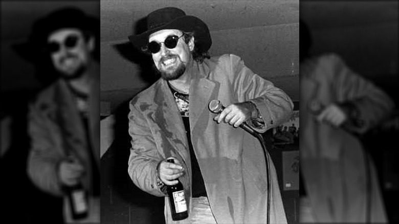 Country Dick Montana sunglasses holding bottle mic on stage