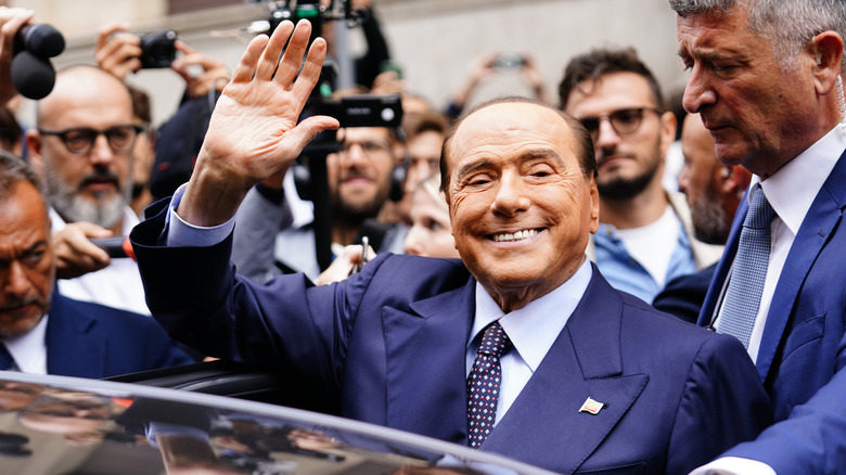 Silvio Berlusconi smiling and waving while entering car