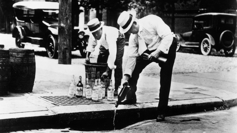 Two men pouring alcohol down a drain in the early 20th century