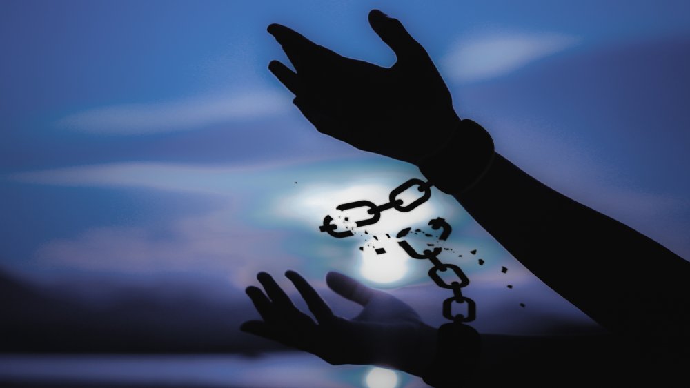 Silhouette of hands breaking chain against a twilight background