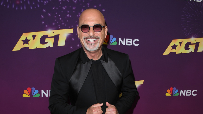 Howie Mandell wearing sunglasses and a black suit and smiling on the red carpet for America's Got Talent