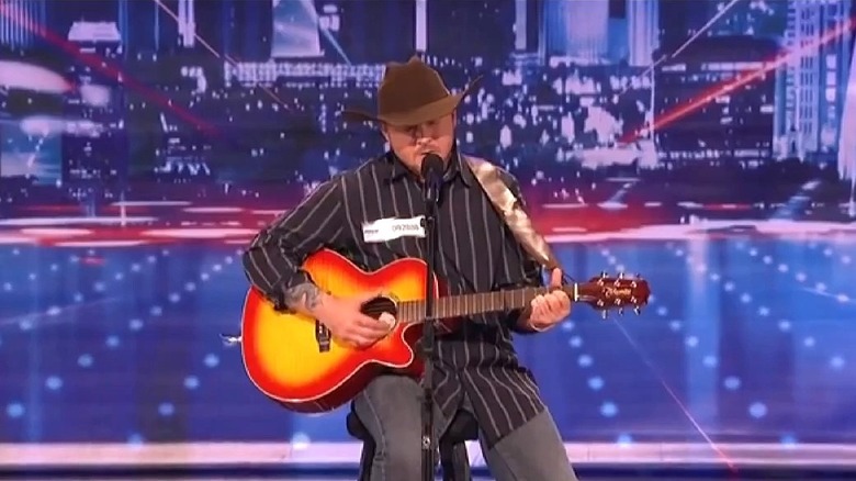 Hat-wearing Timothy Poe playing a guitar and singing on America's Got Talent