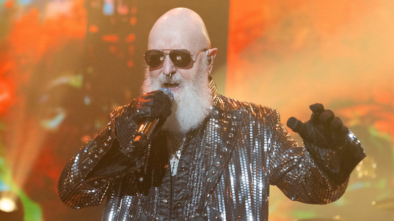 A sunglasses-wearing Rob Halford singing on stage with Judas Priest in 2024