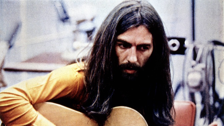 George Harrison with long hair plays acoustic guitar