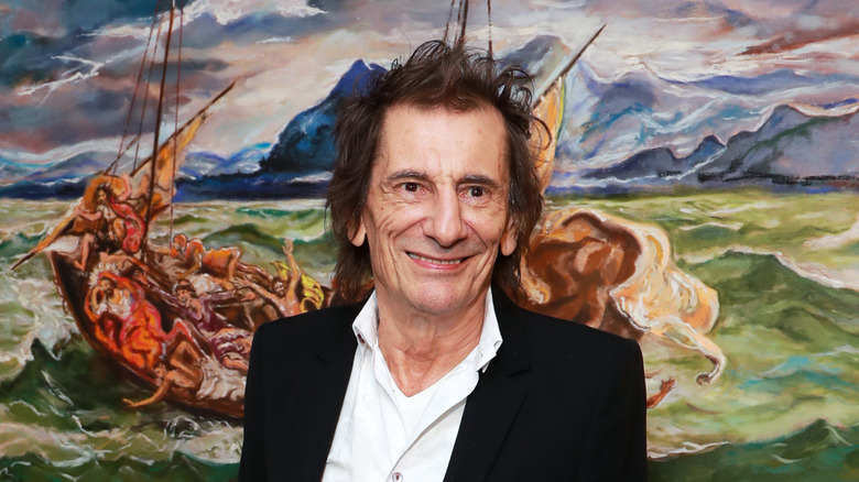 Ronnie Wood posing in front of one of his paintings