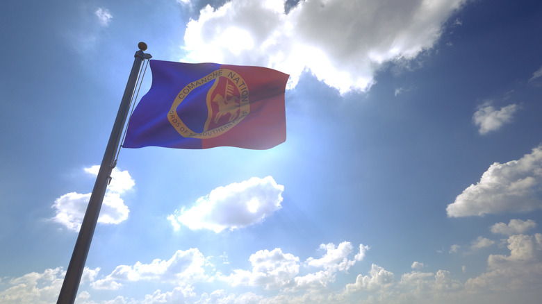 The comanche nation flag waves against a blue sky