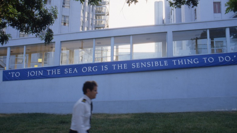 Sea Org Member walks by Sea Org signage