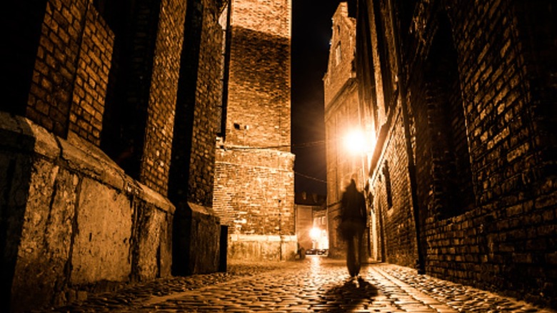 Blurred shadowy figure walking down cobblestone street at night.