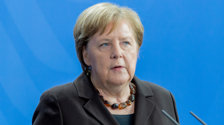 Angela Merkel dark jacket giving speech blue background