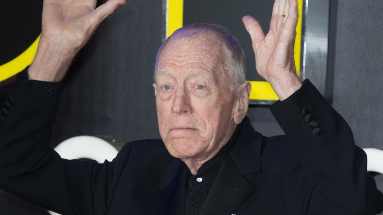 Max von sydow black suit hands raised