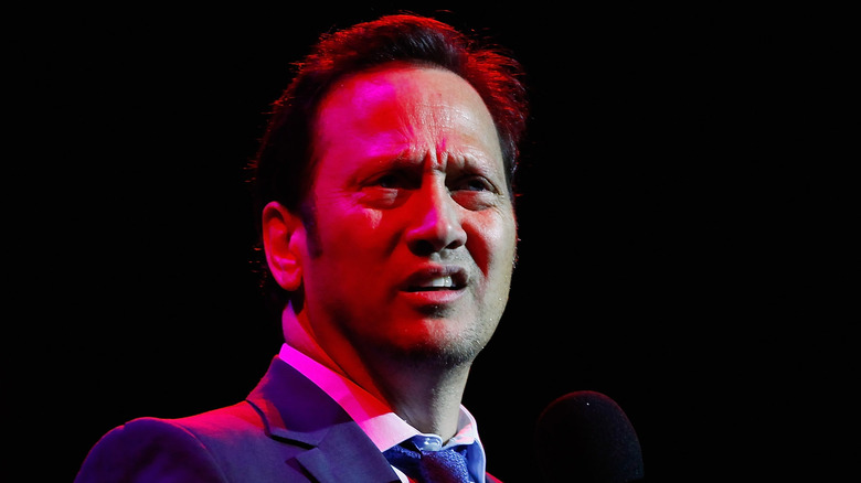 Rob Schneider looking disgruntled holding microphone