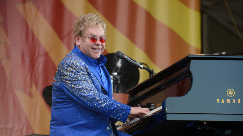 Elton John blue suit red glasses playing piano