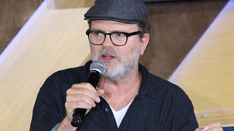 Rainn Wilson glasses cap beard with a microphone