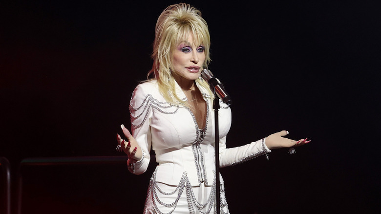 Dolly Parton gesturing while speaking into a microphone onstage