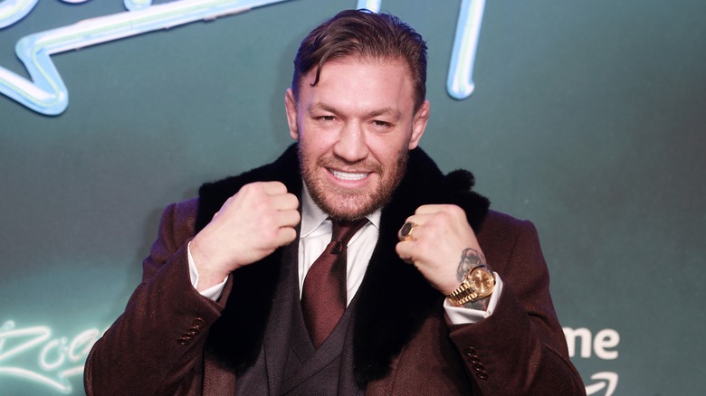 Conor McGregor in brown suit smiling fists up