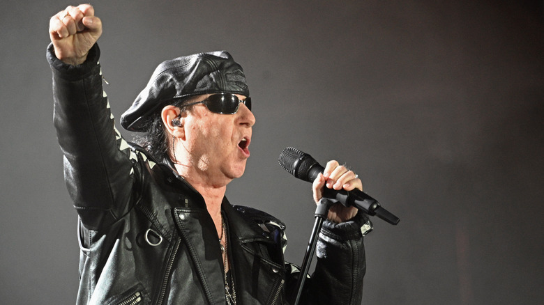 Scorpions' Klaus Meine dressed in all black and holding his fist in the air