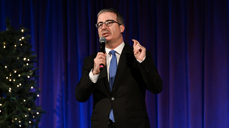 John Oliver black suit glasses standing speaking