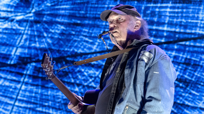 Neil Young denim jacket cap holding guitar