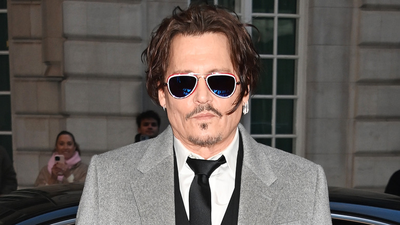 Johnny Depp wearing sunglasses, a grey coat, and black tie