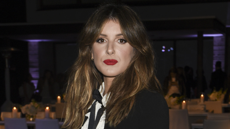 Shenae Grimes wearing a white shirt and black jacket and posing for a photo