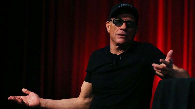 Jean-Claude Van Damme in a cap and sunglasses with red background