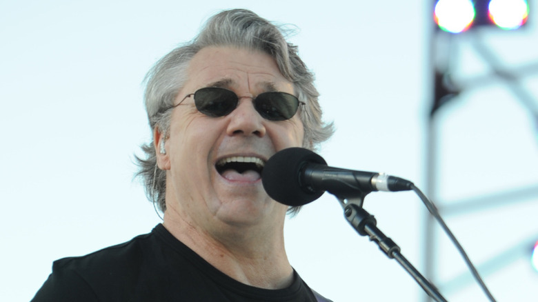 Steve Miller, wearing sunglasses. sings into microphone onstage.