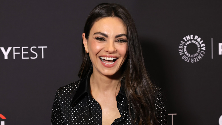 Smiling Mila Kunis wearing a black shirt with white dots