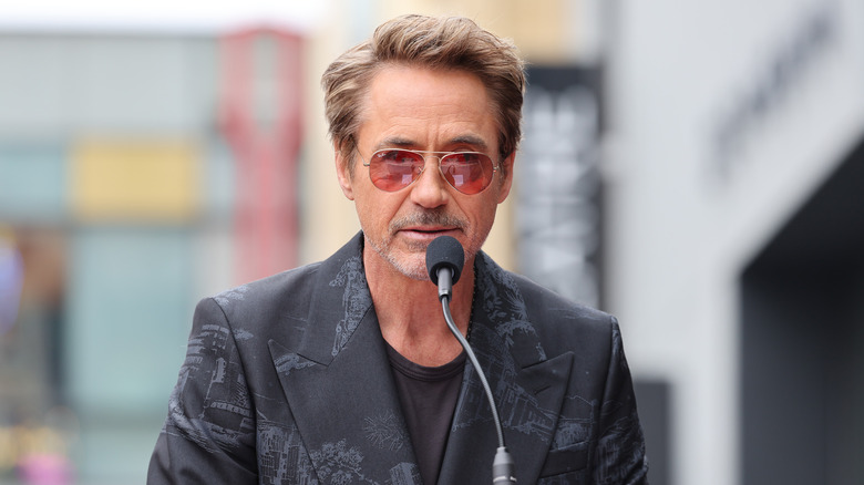 Robert Downey Jr. wearing sunglasses and a blazer as he talks into the mic