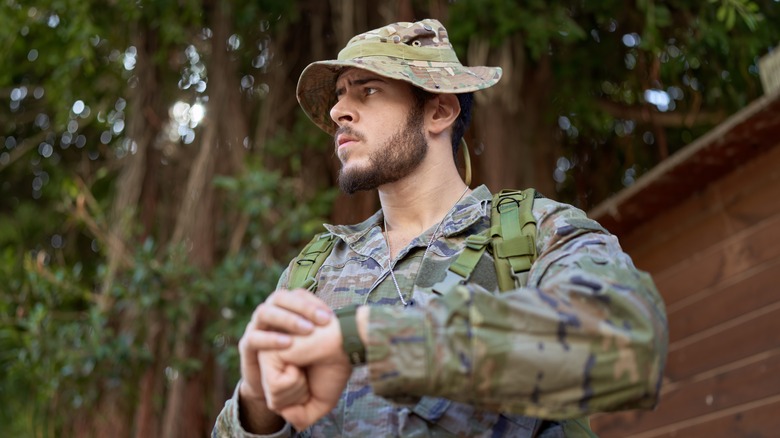 Uniformed hat soldier frowning holding up watch