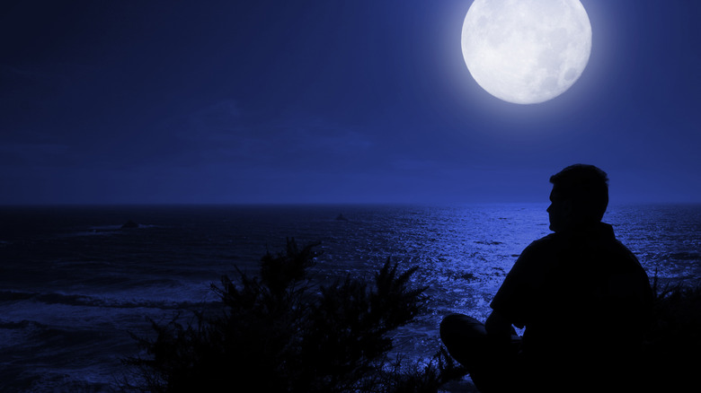 man sitting by the ocean under a full moon