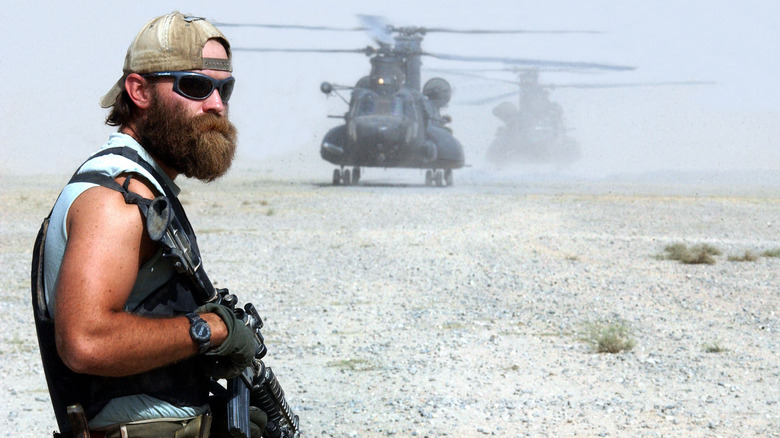 A Green Beret holding a gun standing in front of a helicopter