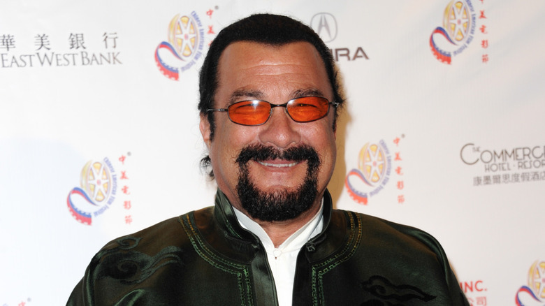 Steven Seagal in a dark green jacket grinning